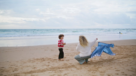 Parent launching kite toy with little boy on beach. Family playing together spending weekend on windy seashore. Young babysitter mom teaching helping kid with flying bird. Carefree childhood concept.の写真素材