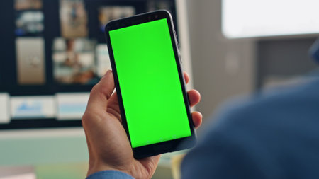 Man hands hold chromakey mobile phone in office closeup. Unrecognizable creator checking messages trading news on green screen device. Unknown designer using smart app. Worker talking virtual callの写真素材