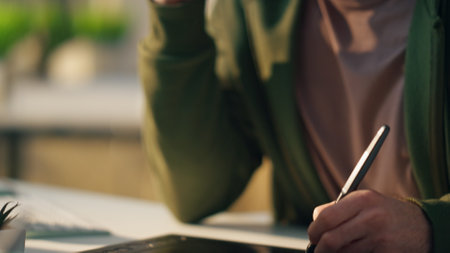 Artist hand drawing stylus on graphic pad at room close up. Serious web designer talking mobile phone at sunny workplace interior. Focused freelance man creator consulting client watching attentivelyの写真素材