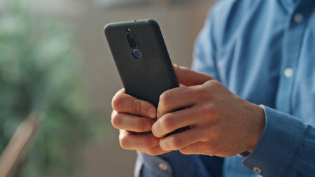 Businessman fingers holding smartphone at cabinet closeup. Unknown man texting business partner at office interior. Financial worker reading news using mobile phone. Startuper hands browsing internetの写真素材