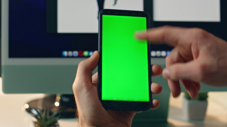 Closeup mockup cellphone scrolling man finger at workplace. Unrecognizable businessman touching chroma key telephone reading news. Manager hand holding greenscreen mobile phone browsing internetの写真素材