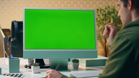 Designer working chromakey computer drawing tablet at office closeup. Focused creator man using green screen pc device holding stylus pen at table workplace. Serious startuper staring mockup monitorの写真素材