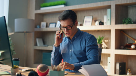 Active man holding telephone call at workplace. Closeup creative startuper calling mobile phone watching computer screen at modern office. Smiling chief designer typing keyboard answering interlocutorの写真素材