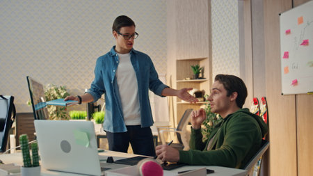 Colleagues discussing project together. Office guys gesturing hands brainstorming in computer table workplace. Emotional web designer talking to colleague at sunny hipster cabinet. Team work conceptの写真素材