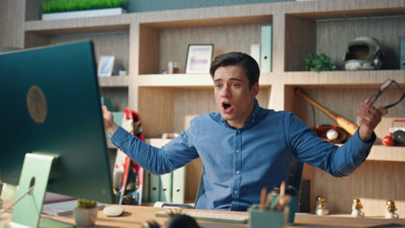 Emotional businessman yelling computer videocall at informal office. Closeup nervous manager gesturing hands speaking video chat. Stressed angry man talking on raised tones arguing at modern workplaceの写真素材