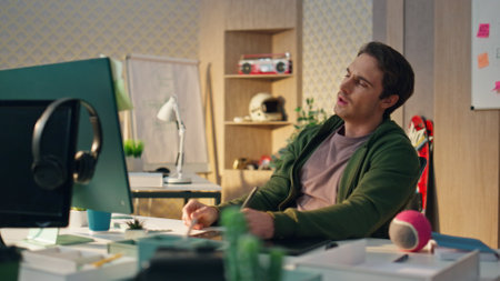 Thoughtful freelancer staring computer screen at office closeup. Graphic designer holding stylus pondering ideas at ecological apartment. Pensive man creating digital art using tablet at cozy studioの写真素材