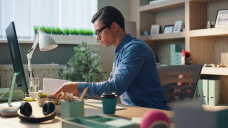 Busy startuper flipping notebook pages at computer table. Close up creative businessman looking for necessary notes sipping coffee at private cabinet. Serious man working calmly at modern office aloneの写真素材