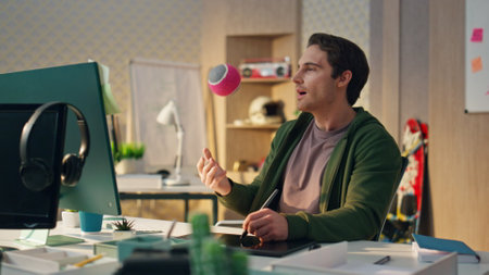 Relaxed guy looking computer screen at creative office. Closeup smiling talented artist drawing tablet display feeling satisfied with results. Positive happy man throwing ball holding digital penの写真素材