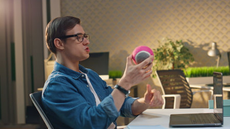 Eyeglasses man tossing toy at computer table closeup. Smiling freelancer catching ball playing with colleague at office moving camera. Two guys giving high five enjoying break in friendly atmosphereの写真素材