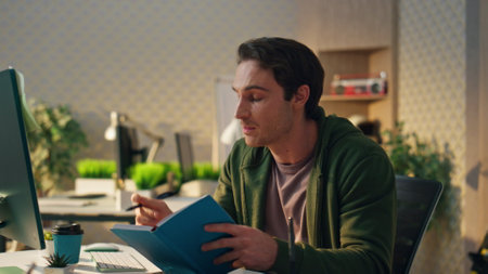 Smart student learning computer video call at home closeup. Smiling thoughtful guy sitting table workplace writing notes in notebook. Freelancer looking for ideas answering questions at online webinarの写真素材