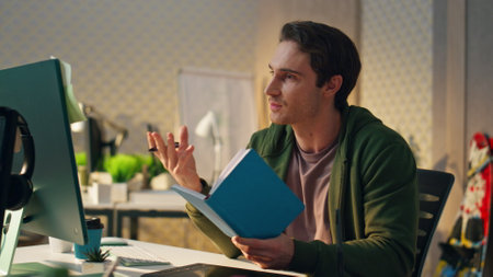 Positive man having virtual call at modern office. Creative business guy discussing project leading presentation on computer online meeting. Smiling freelancer reading notes talking to screen remotelyの写真素材