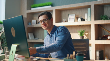 Smiling creator working computer at office closeup. Inspired happy man checking notebook typing pc keyboard at private cabinet. Brunette programmer guy writing code sitting messy work place aloneの写真素材