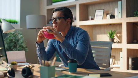 Focused developer staring computer monitor at office table. Closeup serious creator holding ball toy watching pc screen attentively indoors. Eyeglasses freelancer man working at creative space aloneの写真素材