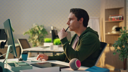 Pensive freelancer watching computer screen at modern office. Closeup graphic designer holding stylus looking for ideas at ecological apartment. Man creating new concept using tablet at design studioの写真素材