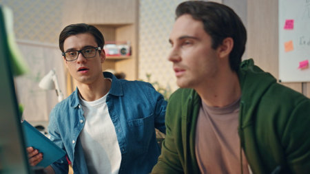 Friendly team working computer together in office room closeup. Confident manager saying opinion supporting teammate. Eyeglasses guy going away brunette man developer looking monitor attentivelyの写真素材