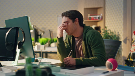 Tired designer rubbing eyes at computer work place. Closeup attentive artist drawing tablet staring monitor in office. Focused overworked creator working desktop pc thinking at late evening cabinetの写真素材