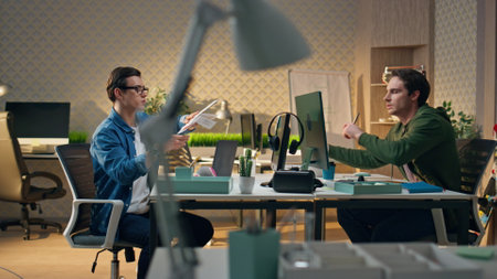 Serious freelancer collaborating colleague at cabinet. Focused web designer giving colour samples to partner at creative space. Young creators working together at office interior. Corporate lifestyleの写真素材