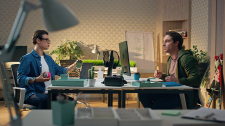 Relaxed men talking office. Two male colleagues drinking beverages enjoying friendly atmosphere. Positive guy playing ball chatting with partner at room. Carefree designers working calmly at cabinetの写真素材