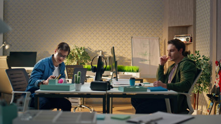 Two people communicating workplace interior. Young team talking at office table. Relaxed colleagues discussing calmly at modern apartment. Positive man drinking tea. Freelance guys finishing workの写真素材
