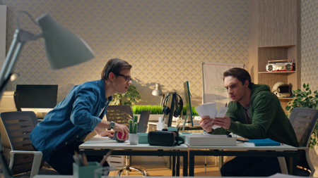 Serious partners advising together at workplace. Focused eyeglasses man talking to male colleague choosing colour at light office table. Creative freelance guys working remotely. Work routine conceptの写真素材