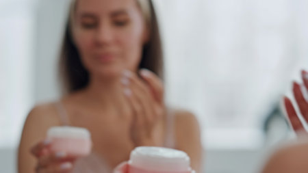 Satisfied model moisturizing face at bath closeup. Grooming lady applying facial foundation holding pink jar at home. Relaxed woman enjoying morning selfcare alone. Professional care product conceptの写真素材