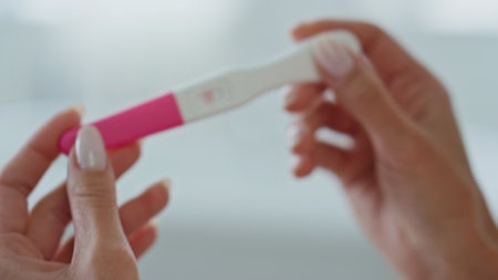 Lady hands pregnancy test holding at home closeup. Unknown woman looking positive result rejoicing in toilet room. Manicure fingers girl expecting kid standing at white place. Future maternity conceptの写真素材