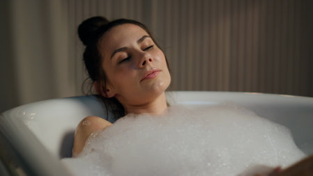 Sensual model enjoying spa routine at evening bathroom. Close up calm woman touching body resting foam bath at home. Sexy gentle lady chilling in bubbles liquid indoors. Beauty procedures conceptの写真素材