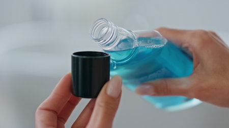 Woman hands pouring mouthwash in cap indoors close up. Unknown lady holding blue antibacterial liquid at bathroom. Unrecognizable girl using refreshing dental rinse. Morning care in bath room conceptの写真素材