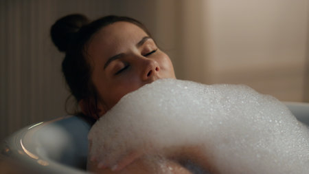 Relaxed woman bathing evening room closeup. Closed eyes sexy girl taking foamy bathtub washing at luxury hotel place. Pretty carefree lady enjoying spa procedure laying hot water at night apartmentの写真素材