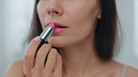 Portrait model applying lipstick at home. Smiling woman putting pink colour enjoying herself zoom out. Closeup pov happy lady making facial makeup using rouge moisturizing lip care at windows placeの写真素材