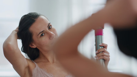 Gorgeous lady drying hair at light room close up. Groomed woman hairstyling in white bathroom. Long haired model using hairdryer at minimalistic interior. Usual morning beauty treatments conceptの写真素材