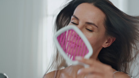 Smiling woman styling hair using hairdryer in bath pov video. Brunette groomed lady drying chevelure at morning home portrait. Satisfied girl looking camera holding hairstyling device at house closeupの写真素材