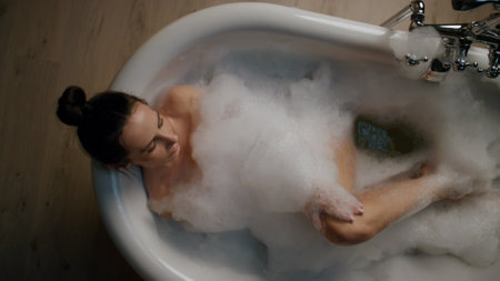Carefree model washing legs in foam bath top view. Relaxed nude girl enjoying beauty routine resting...