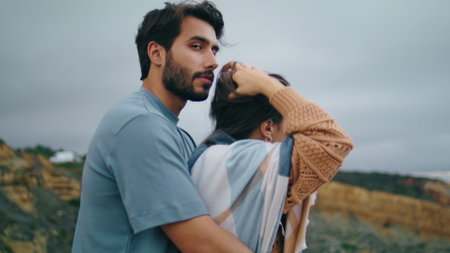 Tender calm couple posing nature standing in front gloomy cloudy sky close up. Handsome bearded man hugging beautiful woman outdoors. Cute loving two people relaxing on weekend vacation together.の写真素材