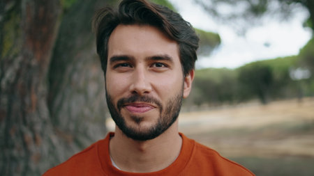 Portrait of happy bearded man looking camera with smile standing beautiful forest alone. Handsome young guy posing on green nature close up. Attractive confident hipster relax on weekend outdoors.の写真素材