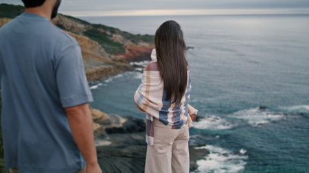 Sensual young couple enjoy sea shore cloudy evening. Attractive bearded man walking to relaxed woman standing on coast hill. Two loving people looking on gloomy seascape hugging. Romantic date conceptの写真素材