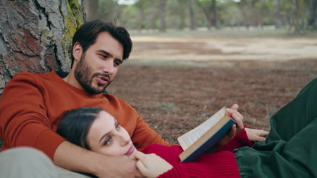 Lovely carefree couple lying park with book closeup. Attractive bearded man reading aloud for beautiful woman. Calm woman relaxing on boyfriend chest. Happy young pair spending time together in forestの写真素材
