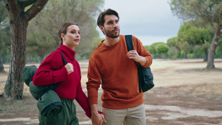 Smiling romantic couple going hike on nature with backpacks. Lovely happy family walking on beautiful autumn forest. Young relaxed tourists enjoy sunny park landscape. Two travelers strolling togetherの写真素材
