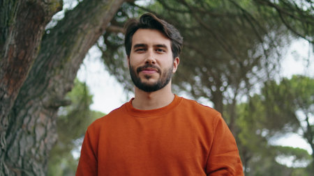 Handsome bearded man smiling to camera in green park close up. Portrait of attractive young guy holding backpack going to trip on nature. Happy tourist standing in front beautiful forest trees alone.の写真素材
