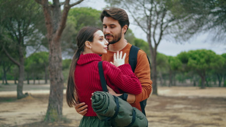 Happy carefree lovers standing in beautiful forest with backpacks close up. Tender young couple travelers hugging on nature feeling love happiness. Relaxed two hikers enjoy closeness outdoors.の写真素材