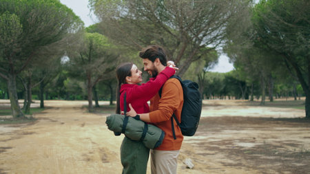 Happy tender couple hugging in front beautiful autumn forest. Lovely cute family embracing standing in nature park. Two travelers in love enjoy hike with backpacks. Calm pair feeling happiness outdoorの写真素材