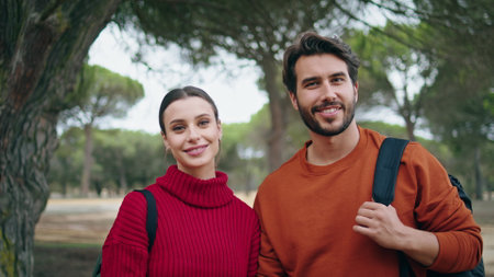Two positive hikers smiling standing in beautiful autumn forest with backpacks close up. Portrait of cheerful young couple feeling joy happiness spending vacation on nature. Family pair relax togetherの写真素材