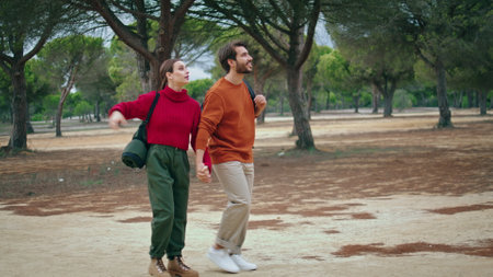 Relaxed carefree travelers walking on forest path looking beautiful nature views. Happy smiling couple strolling on beautiful autumn park with backpacks. Positive young family enjoy active weekend.の写真素材