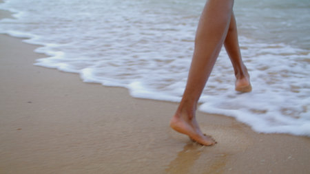 Woman feet walking ocean waves closeup. Unknown playful girl enjoying beach vacation alone. Unrecognized african american tourist splashing playing with sea barefoot. Romantic holiday mood concept.の写真素材