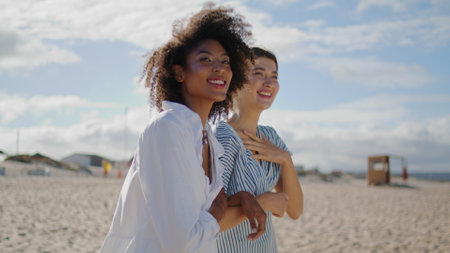 Two girls walking beach on sunny day closeup. Cheerful homosexual couple talking laughing together holding hands. Beautiful multiethnic women enjoy summer vacation at sea shore. Carefree life conceptの写真素材