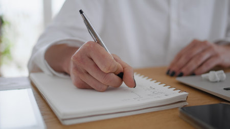 Woman hands writing in notebook at wooden table closeup. Unknown businesswoman holding black ballpen making notes in notepad at office desk. Unrecognizable accountant noting information on paperの写真素材