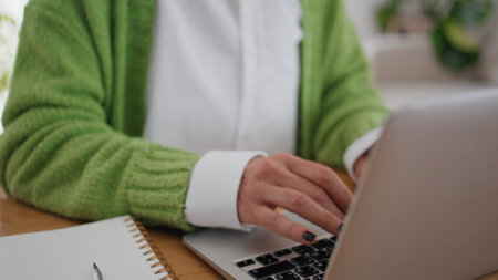 Woman hands typing laptop keyboard at apartment desk closeup. Focused businesswoman working online at modern computer. Thoughtful student girl learning remote texting graduate work at plants interiorの写真素材