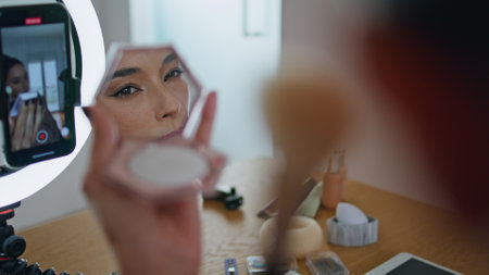 Influencer woman applying makeup looking mirror at house closeup. Beauty blogger putting foundation...