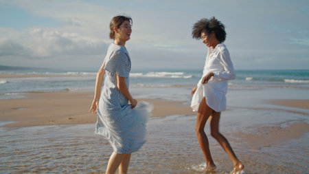 Happy girls dancing beach on summer weekend. Excited smiling lgbt couple enjoy vacation at ocean shore together. Energetic multiethnic women partners having fun on holiday date. Love happiness conceptの写真素材