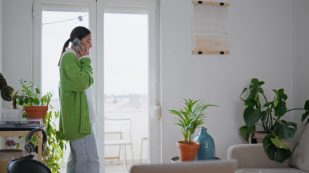 Relaxed girl talking cellphone crossing light house. Calm woman communicating with friend gesturing hand alone at cozy apartment. Focused businesswoman calling telephone explaining information indoorsの写真素材